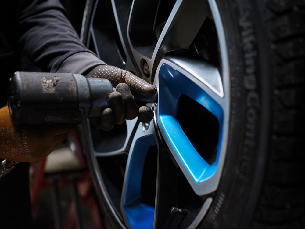 Close up image of a gloved hand and a power drill tightening the bolts on a Lynk & Co car wheel.