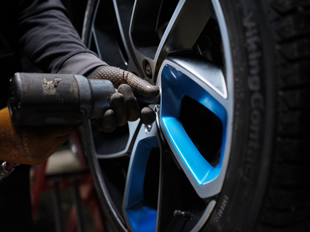 Close up image of a gloved hand and a power drill tightening the bolts on a Lynk & Co car wheel.