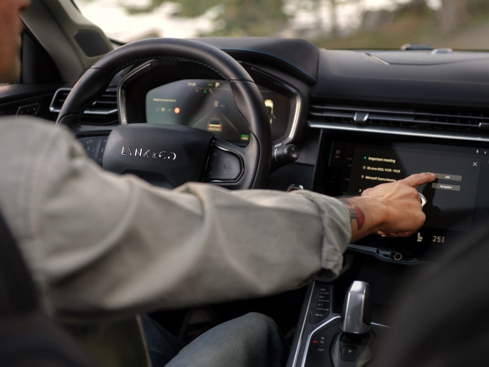 An image of a car dashboard and touchscreen interface. A driver is pressing a button on the screen. 